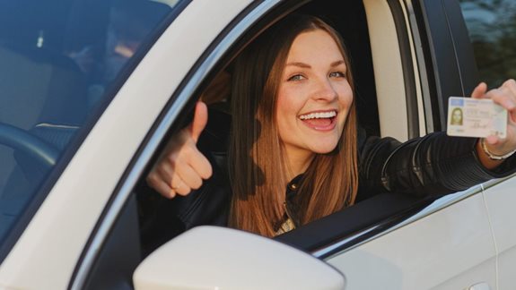 Junge Frau zeigt freudestrahlend ihren Führerschein